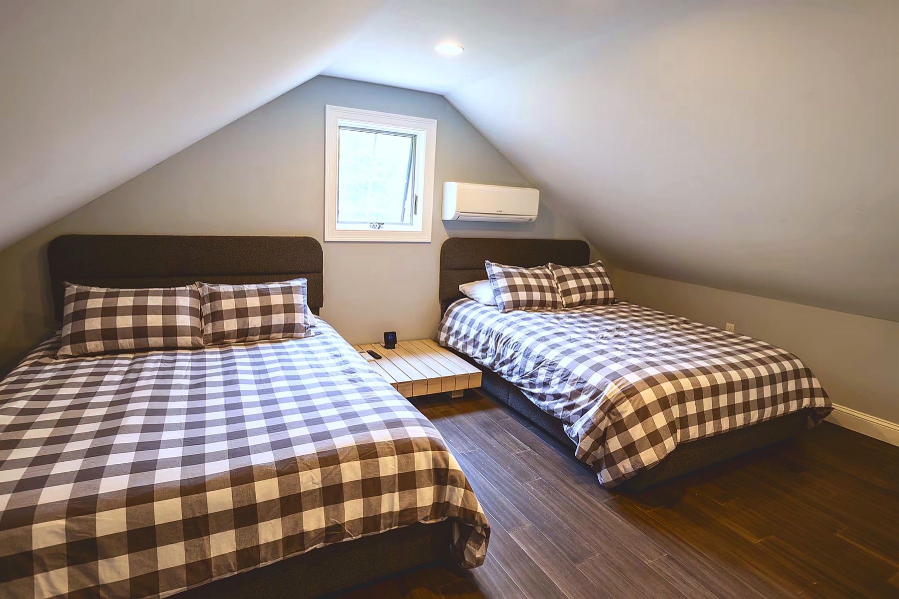 Bedroom with two queen beds in buffalo-plaid bedding under an angled cathedral ceiling