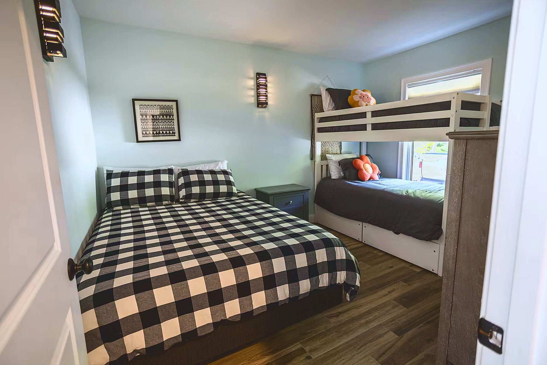 Bedroom with a queen bed in buffalo-plaid bedding and a twin-over-twin bunk bed beside the window