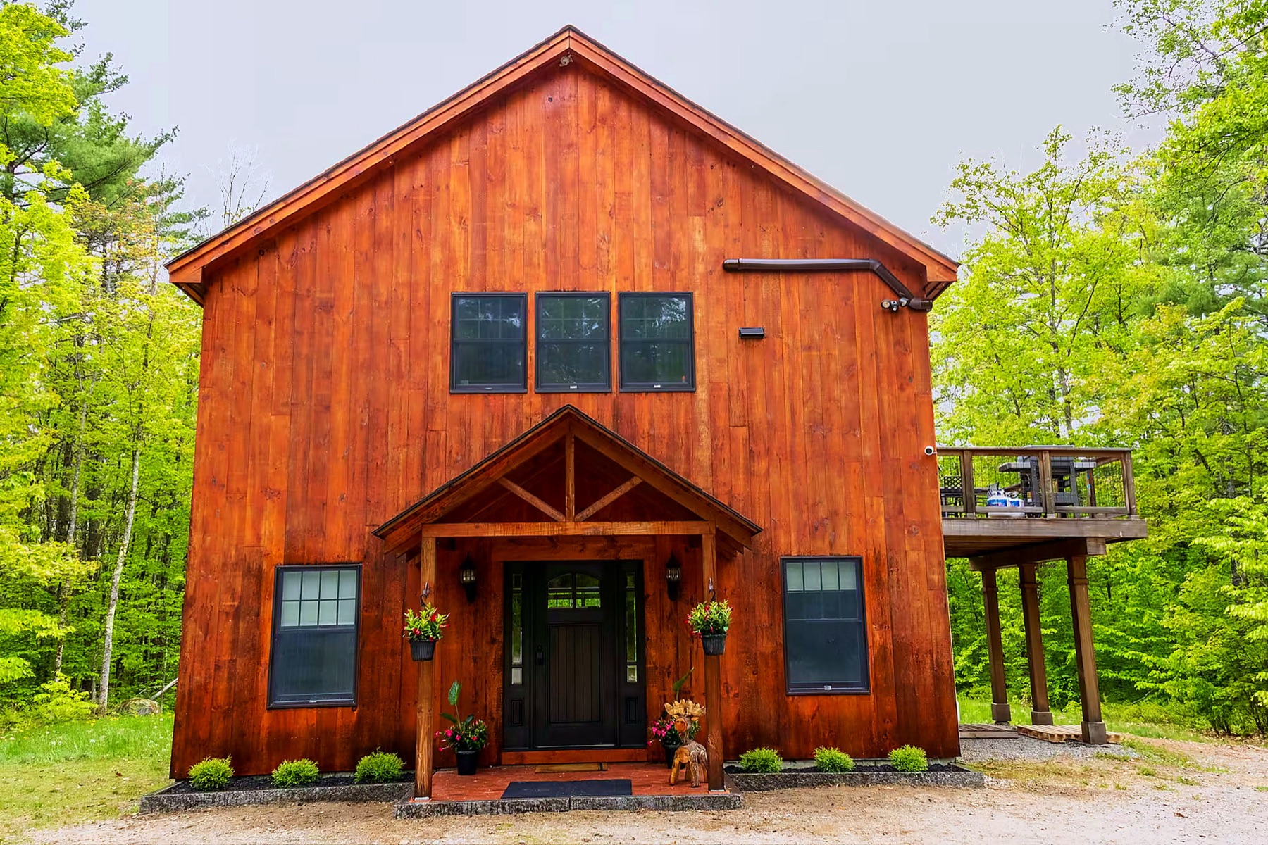 Front exterior of River Run Retreat — a tall, warm-stained timber-frame home set in the woods of Center Conway, NH
