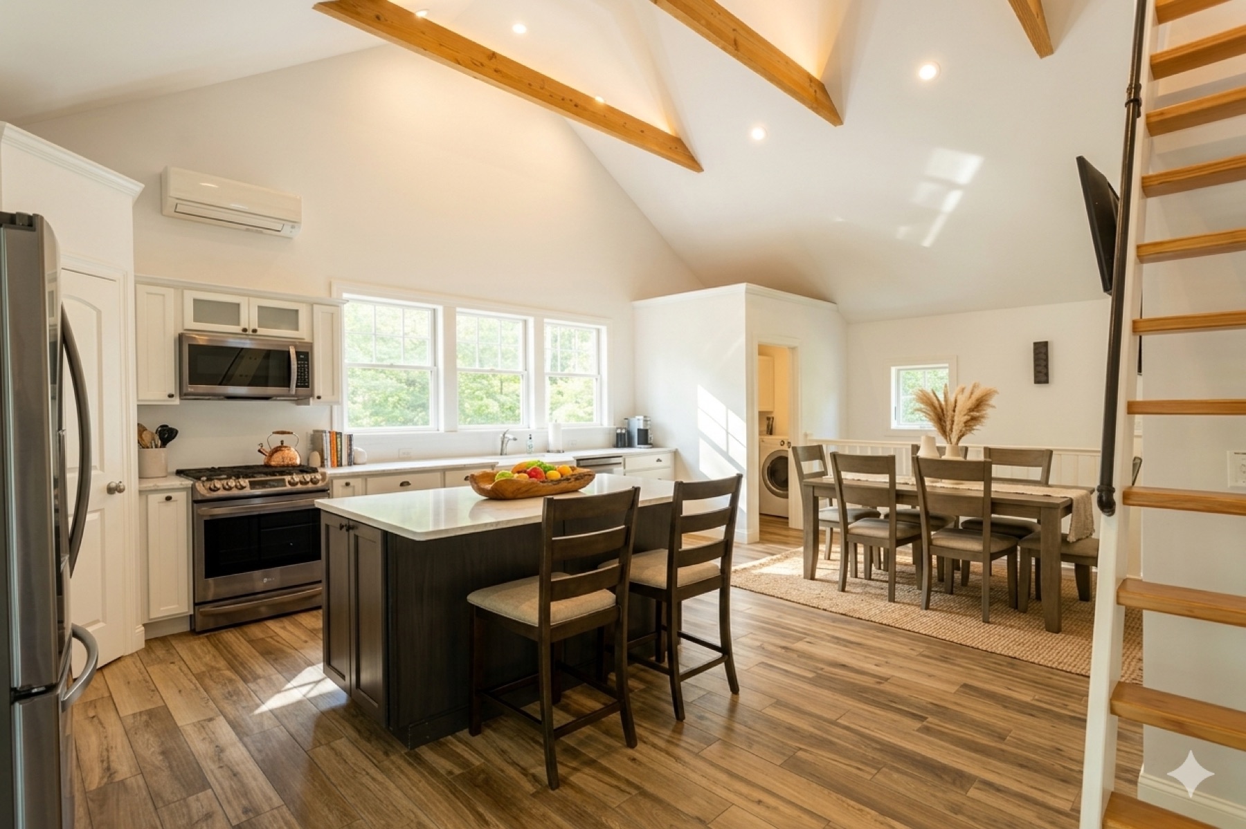 Open-plan kitchen with vaulted beamed ceilings, white cabinets, a dark island with three bar stools, and a dining area in the background